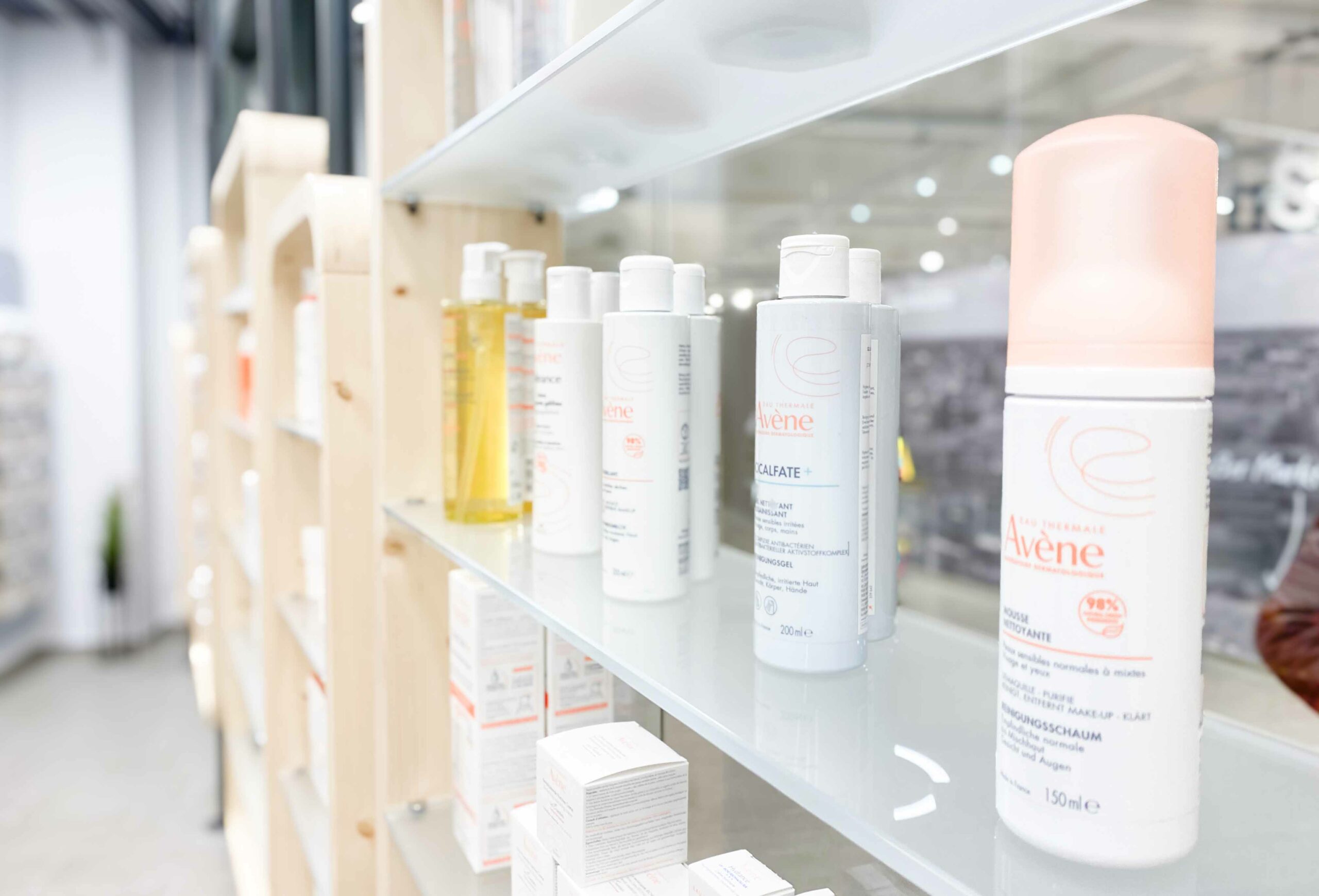 Nahaufnahme eines Glasregals in der Wesel Apotheke der Dr. Kottenberg Apotheken. Im Fokus stehen hochwertige Hautpflegeprodukte der Marke Avène, darunter Reinigungsschaum, Pflegelotion und Duschgel. Die Produkte sind ordentlich sortiert und modern präsentiert.