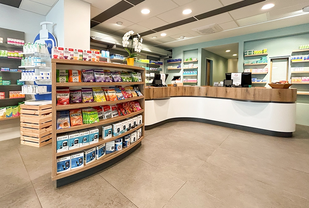 Innenansicht der Bären Apotheke Duisburg: Ein moderner Verkaufsraum mit geschwungenem Holztresen, gut beleuchtetem Kassenbereich und einem Regal mit Em-eukal Bonbons und Gesundheitsprodukten im Vordergrund. Die Rückwand ist mit Apothekenprodukten in farblich sortierten Regalen bestückt.